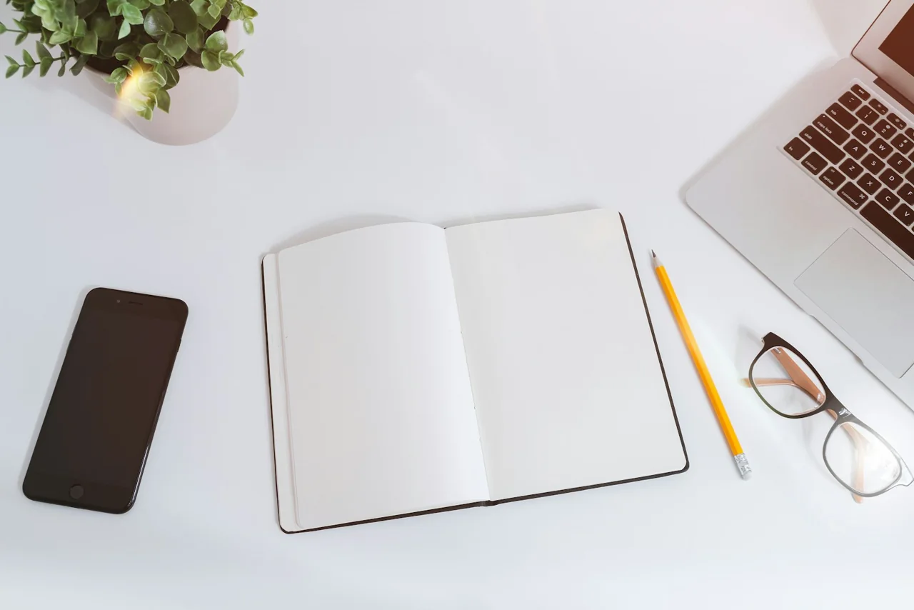 Open notebook, phone and laptop on a bright desk