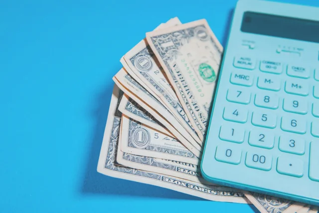 US dollar notes beside a calculator on a blue surface